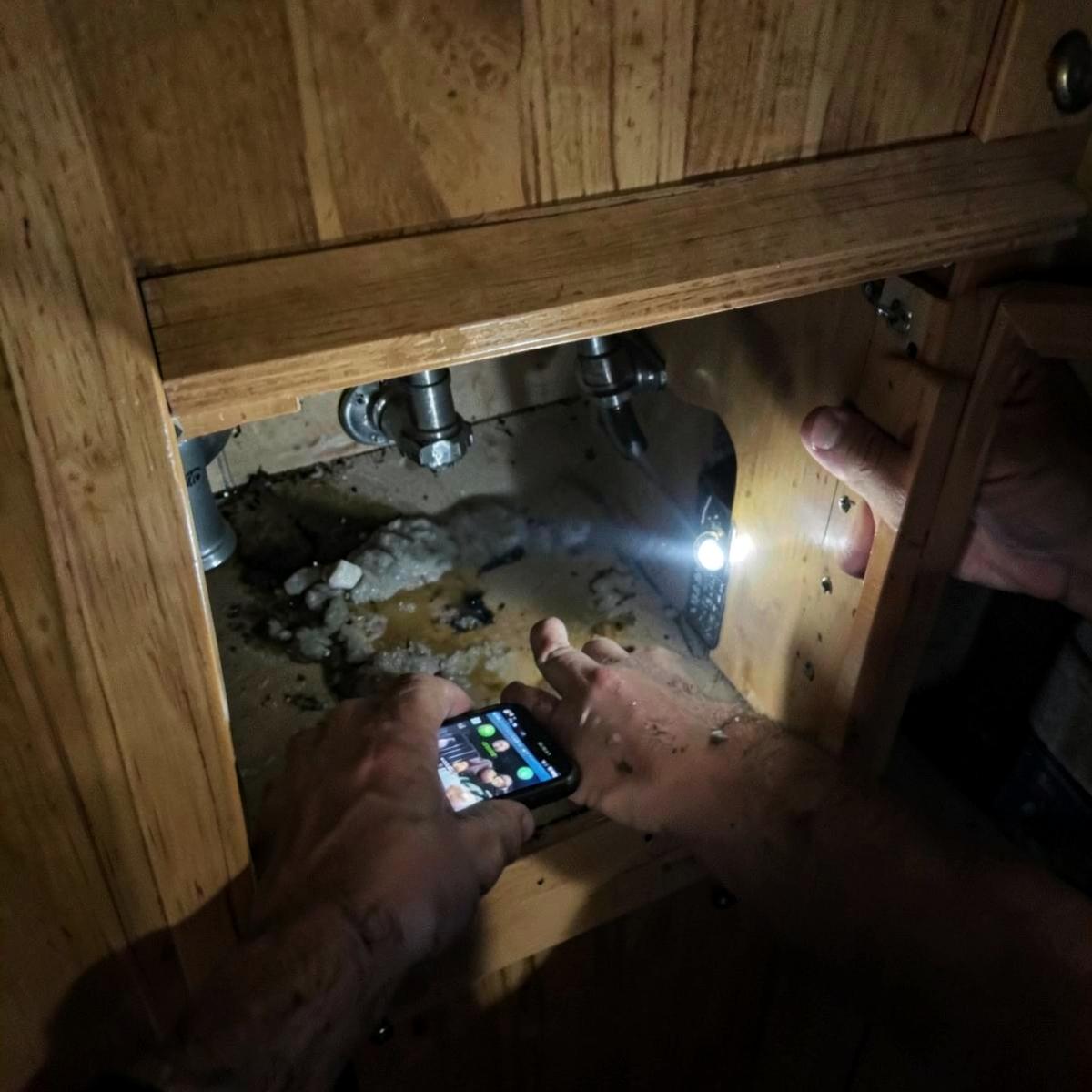 Technician photographing water damage under an RV sink with a flashlight